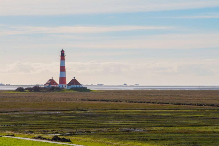 Der Westerhever Leuchtturm mit den Pfahlbauten von St. Peter-Ording am Horizont